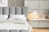 A close-up view of a bed with a plush headboard and white bedding, set against a textured wall. Náhled obrázku produktu