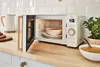 A retro-style microwave oven is shown on a kitchen counter, with its door open to reveal a bowl of soup inside. Other kitchen items like a kettle and bread are also visible. Anteprima dell’immagine prodotto
