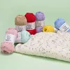 Several balls of yarn in various colors are arranged around a knitted garment, all on a light green background. Produktbild-Vorschau