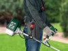 A person wearing a plaid shirt and jeans is holding a gas-powered string trimmer in a grassy outdoor area. Produktbild-Vorschau