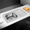 A stainless steel kitchen sink with a draining board is shown on a white countertop. Produktbild-Vorschau
