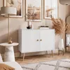 A white two-door cabinet with wooden legs, decorated with a lamp, artwork, and dried flowers in a room. Produktbild-Vorschau