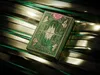 A green and gold deck of cards with intricate designs, resting on a reflective surface with green and gold stripes. Náhled obrázku produktu