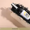 A bottle of wine is presented in a wooden box with black shredded paper. Produktbild-Vorschau