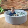 A young boy is playing in a ball pit filled with colorful balls. Produktbild-Vorschau