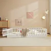 A white wooden children's bed with a guardrail is set up in a room with light beige walls and a cream rug. Náhľad obrázku produktu