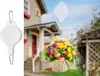 A hanging basket of flowers is suspended from a retractable plant hook, with a house in the background. Náhled obrázku produktu