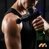 A person using a massage gun on their shoulder in a gym-like setting. Produktbild-Vorschau