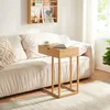 A wooden laptop table with a drawer is placed next to a sofa, with a laptop and a cup on it. Náhled obrázku produktu