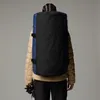 A person wearing a tan puffer jacket and black pants, viewed from the back, is wearing a large blue and black duffel bag backpack. Voir les images du produit