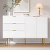 A white sideboard with gold accents and fluted detailing, set against a wall with vertical stripes and a framed abstract artwork. Podgląd zdjęcia produktu