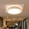 A modern, circular ceiling light fixture with a white matte finish, mounted on a white square base, illuminating a hallway. Náhled obrázku produktu