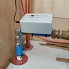 A water conditioner device is installed on copper pipes in a room with wooden walls and a light gray floor. Anteprima dell’immagine prodotto