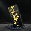 A black phone case with a gold butterfly design is shown at an angle, with a blue glow emanating from its base and debris scattered around it. Produktbild-Vorschau