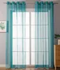 A pair of sheer turquoise curtains hanging in front of a window with a grid pattern. A framed picture of greenery is visible on the left, and a wooden dresser with a plant is on the right. Produktbild-Vorschau