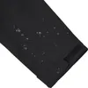 A close-up view of a black jacket sleeve with water droplets on it, showing its water-repellent properties. A velcro strap is visible at the cuff. Produktbild-Vorschau