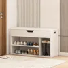 A white shoe cabinet with storage shelves and a drawer, filled with shoes and boots, placed in a hallway next to a door. Produktbild-Vorschau