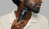 A man is trimming his beard with a black electric trimmer. Produktbild-Vorschau