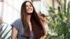 A young woman with long brown hair smiles and touches her hair while walking outdoors. Voir les images du produit