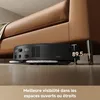 A black robot vacuum cleaner is shown cleaning the floor next to a brown sofa. Voir les images du produit