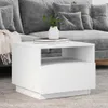 A white side table with a vase and books on top, placed in front of a grey sofa. Voir les images du produit