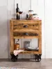 A wooden side table with two drawers and an open shelf, styled with a wine bottle, glass, jars of nuts, a coffee grinder, and plates. Produktbild-Vorschau