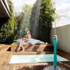 A woman is showering outdoors next to a small pool, sitting on a wooden platform. Produktbild-Vorschau