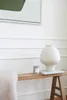 A minimalist interior scene featuring a wooden console table with a large white vase and a candle on it, against a white wall with decorative molding. A textured throw blanket is visible on the left. Anteprima dell’immagine prodotto