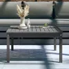 A square wooden coffee table with a slatted top, placed on a rug in an outdoor setting with a sofa in the background. Podgląd zdjęcia produktu