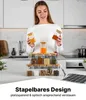 Frau hält zwei quadratische Glas-Gewürzgläser mit Bambusdeckeln, mit einem Set von zehn weiteren Gläsern gefüllt mit Gewürzen auf einer Küchentheke, neben einem Kreidestift und Etiketten Anteprima dell’immagine prodotto