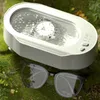 A white ultrasonic cleaner is shown in a natural outdoor setting with green moss and plants, with a pair of glasses placed in front of it. Produktbild-Vorschau