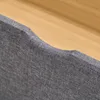 A close-up view of the edge of a gray fabric bed frame with a wooden surface behind it. Produktbild-Vorschau