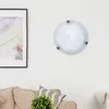 A ceiling light fixture is mounted on a white wall above a sofa. Produktbild-Vorschau