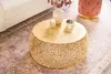 A gold coffee table with a decorative base is placed on a rug in a living room setting. A white vase with red berries and a lit candle are on the table. Produktbild-Vorschau