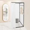 A freestanding changing room with a white curtain and a beige shirt hanging on a rack, next to a large oval mirror. Voir les images du produit