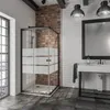 A modern bathroom with a black-framed glass shower enclosure, a white sink with a black faucet, and exposed brick and white subway tile walls. Produktbild-Vorschau