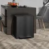 A black pedal trash can is placed next to a dark wood kitchen island in a modern home setting. Voir les images du produit