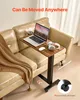 A mobile side table with a laptop, headphones, and a cup is placed next to a sofa. Produktbild-Vorschau
