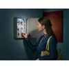 A woman is reaching for keys from a lit key cabinet mounted on a wall. Podgląd zdjęcia produktu