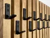 A close-up view of multiple black metal hooks mounted on a wooden slat wall. Náhled obrázku produktu