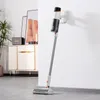 A cordless vacuum cleaner is mounted on a wall charger in a room with a cabinet and artwork. Produktbild-Vorschau