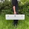 A person is holding a silver case in a grassy outdoor setting. Produktbild-Vorschau