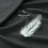 A close-up shot of a dark gray fabric, likely a bedsheet, with a white feather resting on it. Text overlays indicate softness and coziness. Produktbild-Vorschau