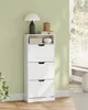A white shoe cabinet with three flip-down drawers is shown in a room with a light green wall. Náhled obrázku produktu