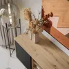 A close-up view of a TV cabinet with dried flowers and a large lamp in a modern interior setting. Produktbild-Vorschau