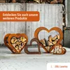 Several heart-shaped metal log holders filled with firewood are displayed outdoors in front of a wooden wall. Produktbild-Vorschau