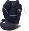 A dark blue car seat with gray accents and green highlights, shown from a three-quarter front angle against a white background. There are graphic elements indicating sound waves emanating from the side of the seat. Náhľad obrázku produktu