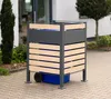 A trash can enclosure with a blue bin inside, placed on a paved driveway in front of a building. Náhled obrázku produktu