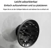 A close-up of a black hair dryer diffuser attachment mounted on a textured wall. Produktbild-Vorschau