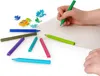 A child's hand is drawing on a piece of paper with a green pencil, surrounded by other colored pencils and small dinosaur-shaped erasers. Anteprima dell’immagine prodotto